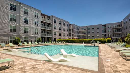 A large swimming pool surrounded by lounge chairs and apartment buildings.