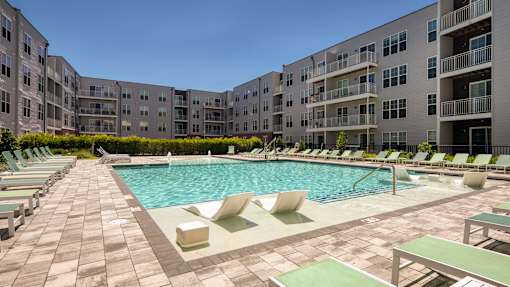 A large outdoor swimming pool surrounded by lounge chairs and buildings.