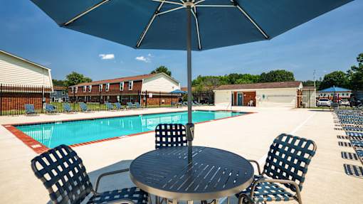 A table with chairs and an umbrella is in front of a pool.