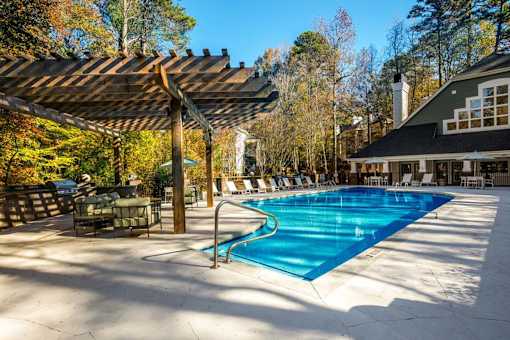 A large outdoor swimming pool with a wooden pergola over it.