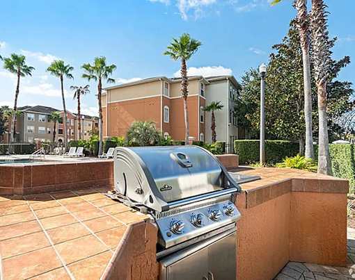 A grill is on a patio with a building and palm trees in the background.