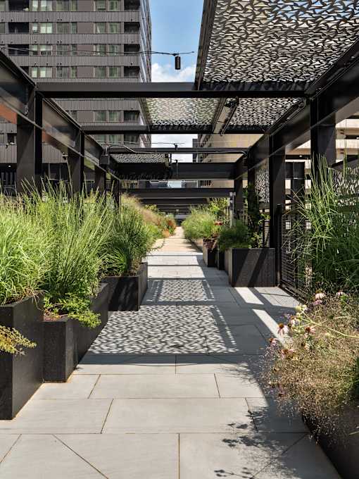 A walkway with a metal roof and concrete planters on either side.