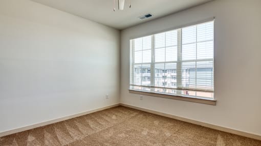 an empty living room with a large window and carpeting