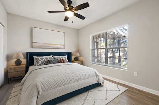 A bedroom with a large bed, a ceiling fan, and a window with blinds.