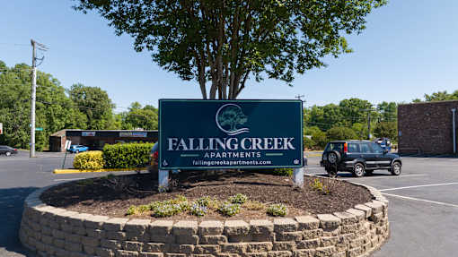 A sign for Falling Creek Apartments is displayed in front of a tree and a parking lot.