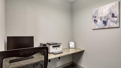 A room with a desk, chair, and a painting on the wall.