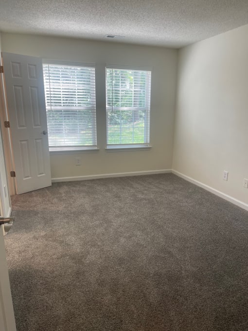 a carpeted room with two windows and a door