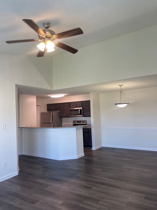 an empty living room with a ceiling fan and a kitchen