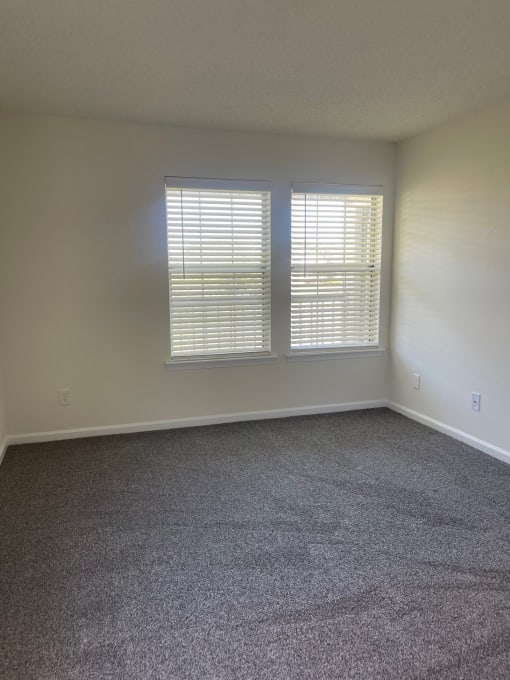 an empty living room with two windows and carpet