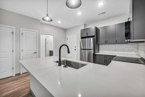 A modern kitchen with a long white countertop and stainless steel appliances.