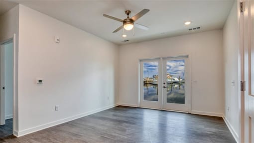 an empty living room with a ceiling fan and large windows at The Port at East Beach Apartments and Marina, Norkfolk