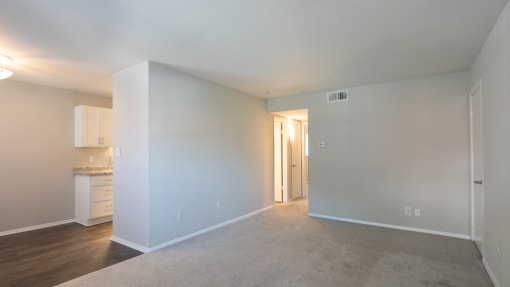an empty living room with a kitchen in the background