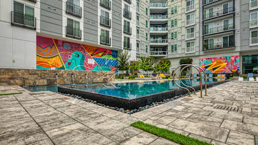A pool surrounded by a concrete patio and a colorful mural on the wall.