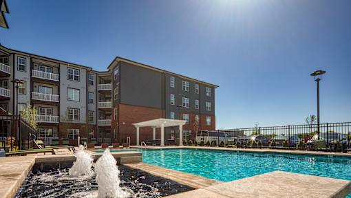 A sunny day at a pool with a fountain in the foreground and apartment buildings in the background.