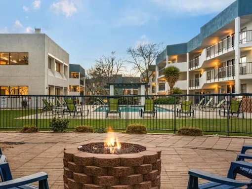 A fire pit sits in the middle of a patio surrounded by chairs and tables.