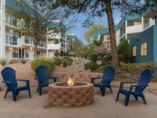 A fire pit surrounded by blue chairs in front of apartment buildings.
