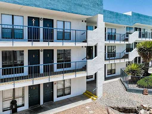 A white building with black doors and windows has a balcony with a yellow railing.