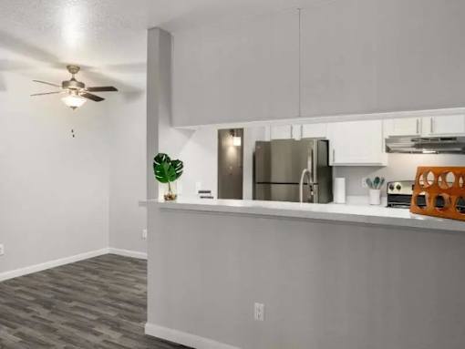 A kitchen with a refrigerator, ceiling fan, and a counter with a plant and a toaster on it.