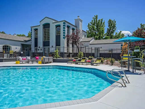 A large swimming pool in front of a house with a deck and lounge chairs.