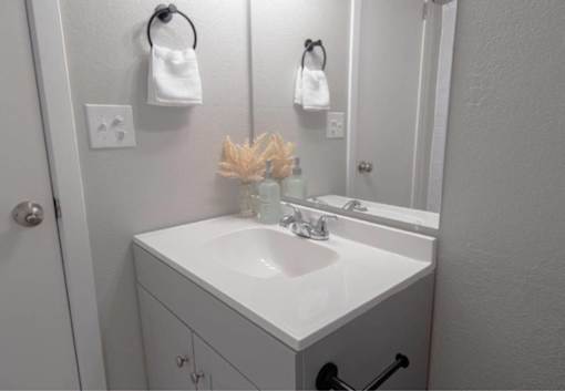 A white bathroom sink with a vase of dried flowers on top.
