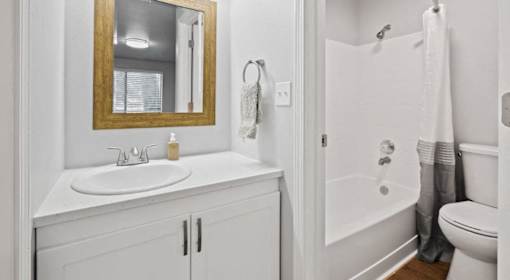 A white bathroom with a sink, mirror, and bathtub.