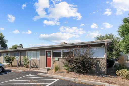 A building with a red door and a parking lot in front.