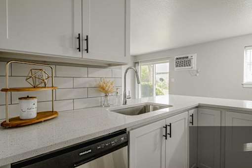 A kitchen with a black dishwasher and white cabinets.