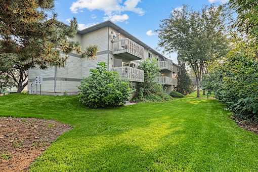 A grassy area in front of a building with trees and bushes.