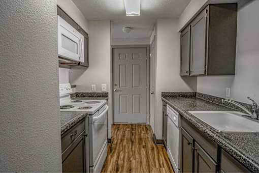 A kitchen with a white oven and microwave, a white door, and a white sink.