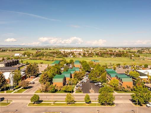 A large green and brown building complex with a parking lot in front.