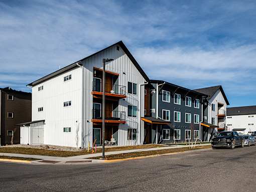 A modern multi-story building with a white and grey exterior and a black car parked in front.