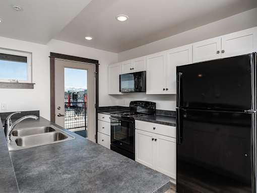 A black refrigerator is in a kitchen with white cabinets.