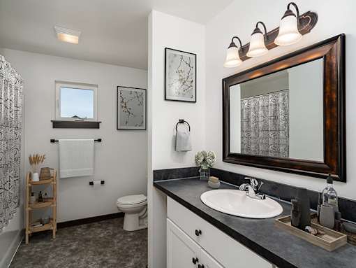 A bathroom with a toilet, sink, mirror, and a window.