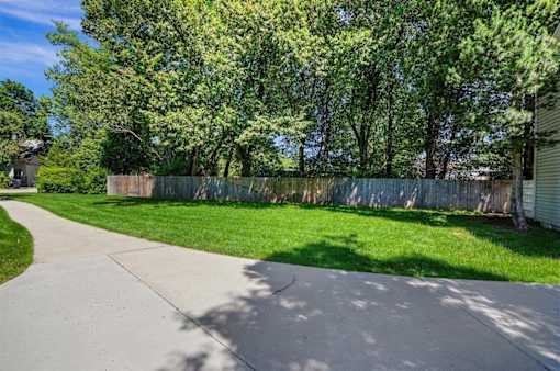 A concrete pathway leads through a grassy area with a fence and trees in the background.