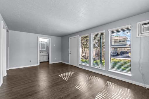 A room with wooden floors and white walls, with a window showing a view of a building outside.