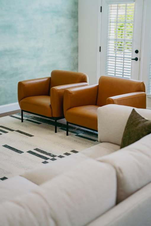 Two brown leather chairs and a white couch in a room.