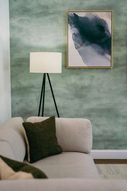 A white couch with a green pillow and a painting on the wall.