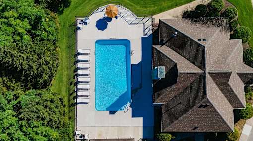 A swimming pool surrounded by a concrete deck and a house with a brown roof.