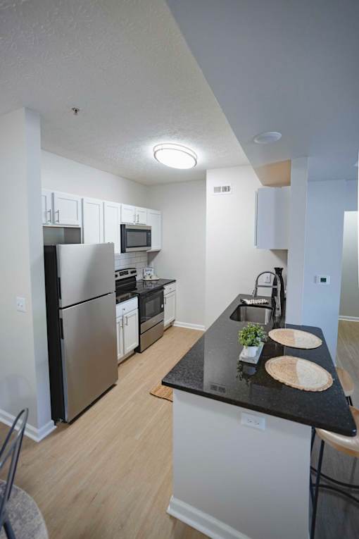 A kitchen with a black counter top and stainless steel appliances.