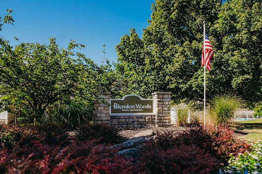 A sign that says Blendon Woods is in front of a flag.