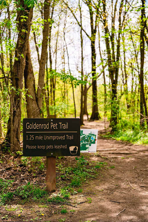 A trail sign for the Goldenrod Pet Trail is displayed in a wooded area.