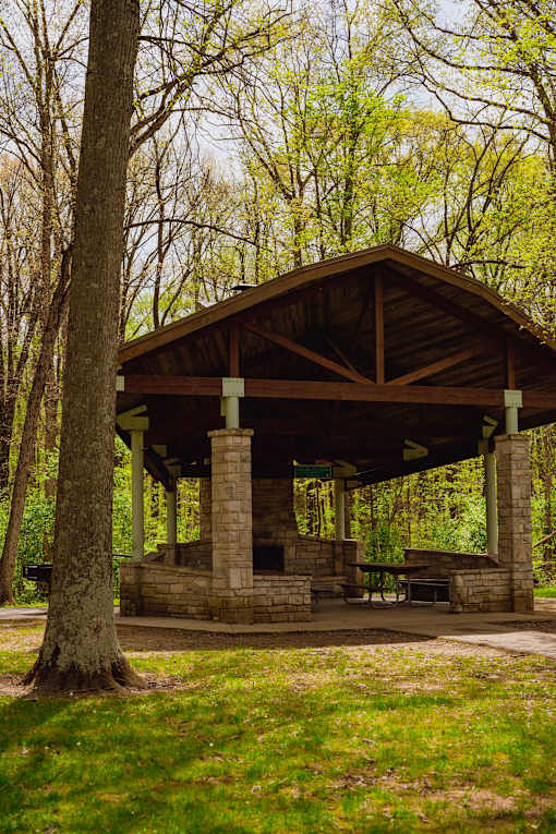 A pavilion with a stone base and a wooden roof is surrounded by trees.