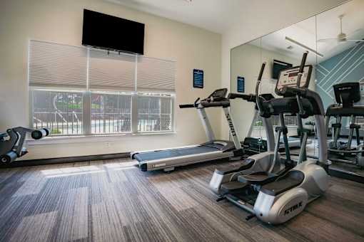A gym with treadmills, elliptical machines, and a flat screen TV.