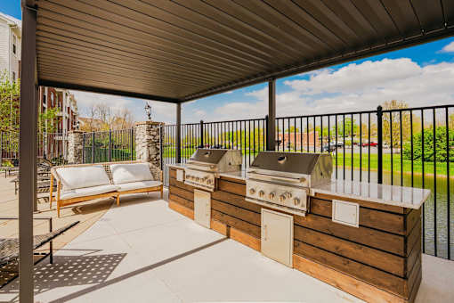 A patio with a grill and a couch under a roof.
