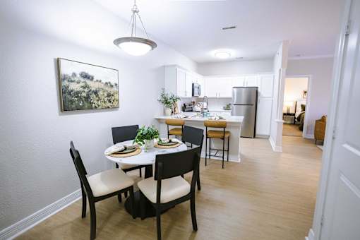 A dining room with a table set for two and a kitchen in the background.