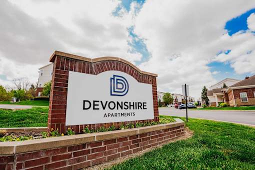 A sign for Devonshire Apartments is displayed in front of a grassy area.