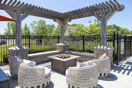 A patio with a fire pit and chairs under a pergola.