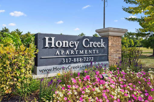 A sign for Honey Creek Apartments is surrounded by flowers.