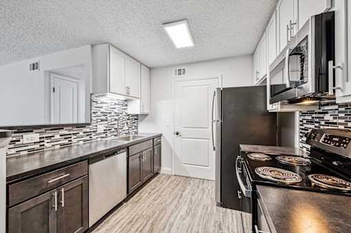 A kitchen with a black refrigerator and wooden floors.