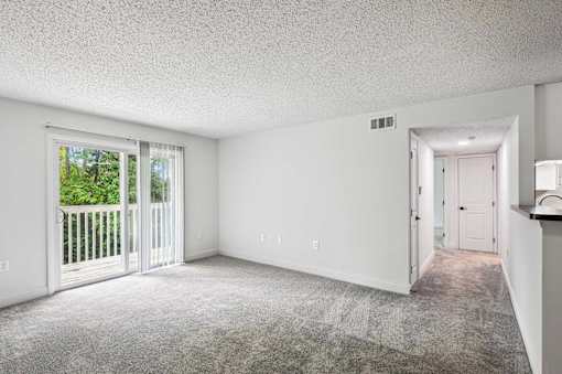 A sparsely furnished room with a carpeted floor and a sliding glass door leading to a balcony.